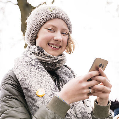 Sternsinger-Begleiterin lächelt mit Handy in der Hand in die Kamera.