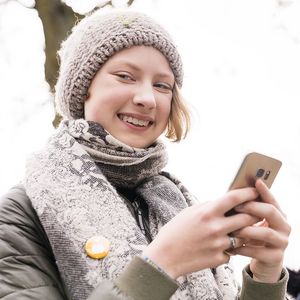 Sternsinger-Begleiterin lächelt mit Handy in der Hand in die Kamera.