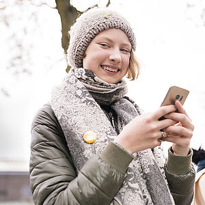 Sternsinger-Begleiterin lächelt mit Handy in der Hand in die Kamera.