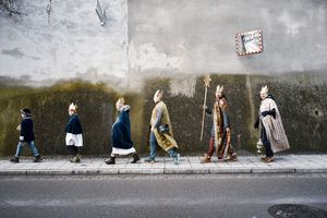 Sechs Sternsinger laufen vo einer Wand. Alle tragen Umhänge und Kronen, und einer hat einen Stern in der Hand.